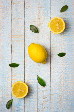 Flat lay composition of ripe whole and half lemons with leaves on light blue wooden background. Copy space, top view.の写真素材