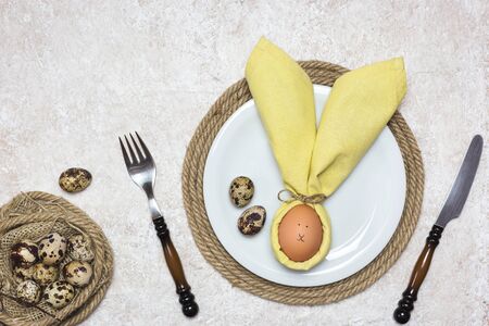 Beautiful festive Easter table setting with egg in napkin like Easter Bunny and quail eggs on light...