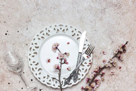 Beautiful festive table setting with spring blossoming branches on light textured background. Top...