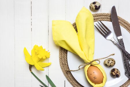 Beautiful festive Easter table setting with egg in napkin like Easter Bunny and spring flowers on...