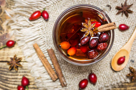 Close-up photo of cup of tea with rose hips and spices on rustic wooden background, top view. Autumn vitamin drink.の写真素材