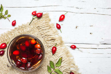 Close-up photo of cup of tea with rose hips on rustic wooden background, top view. Autumn vitamin drink.の写真素材