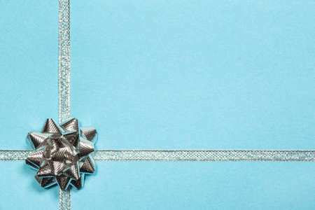 Shiny silver ribbon and gift bow on pastel blue background. Christmas, New Year, Valentine's day or...