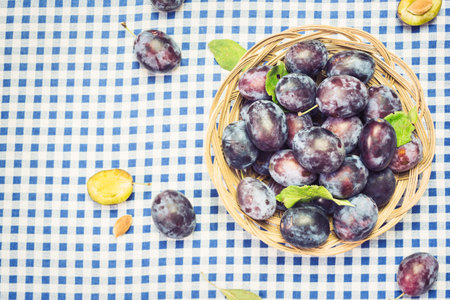 Lot of fresh organic plums in wooden basket with leaves, top view with space for text. Healthy fruits.の写真素材