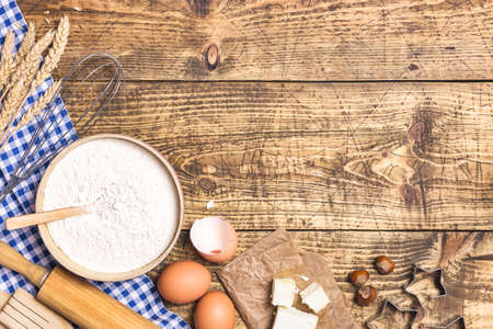 Frame of baking and cooking pastry or cake with ingredients and utensils. Eggs, hazelnuts, butter, flour and wheat on rustic wooden background with copy space for text, flat lay.の写真素材
