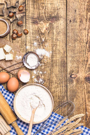 Frame of baking and cooking pastry or cake with ingredients and utensils. Eggs, hazelnuts, butter, flour and wheat on rustic wooden background with copy space for text, flat lay.の写真素材