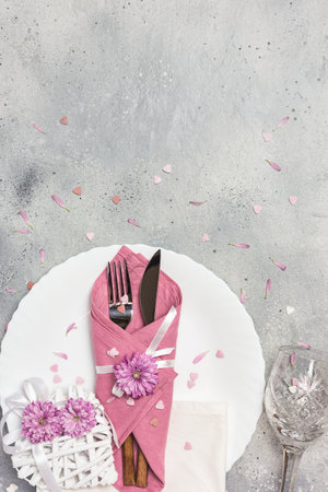 Beautiful festive table setting with white plate, napkin, flowers and hearts decoration on gray stone background. Top view with copy space.の写真素材