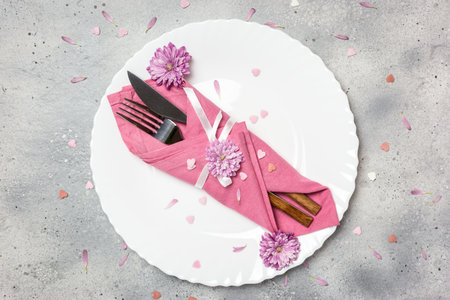 Beautiful festive table setting with white plate, napkin, flowers and hearts decoration on gray stone background. Top view with copy space.の写真素材