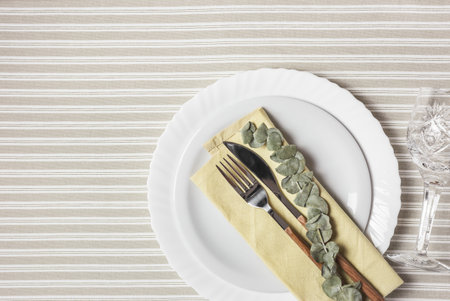 Festive table setting with white plate, cutlery and yellow napkin. Beautiful flat lay arrangement.の写真素材