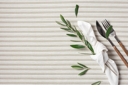 Beautiful flat lay arrangement with cutlery, white napkin and decoration with olive branches. Festive table setting.の写真素材