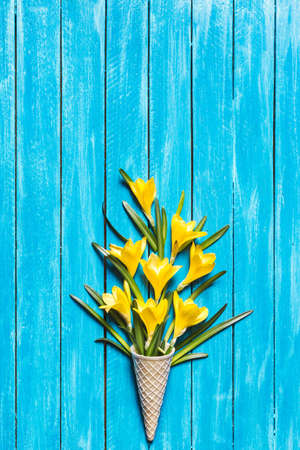 Yellow flowers in ice cream cone on a turquoise wooden background. Spring minimal concept. Flat lay.の写真素材