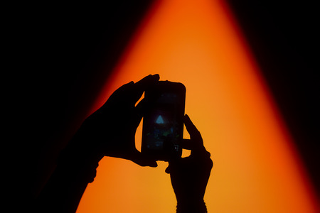 Silhouette of hands taking a photo with mobile phone on a concert with bright stage lights