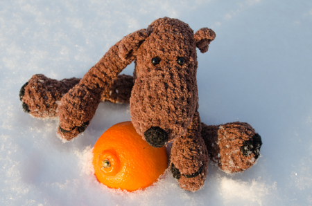 toy teddy bear sitting in the snow with a tangerineの写真素材