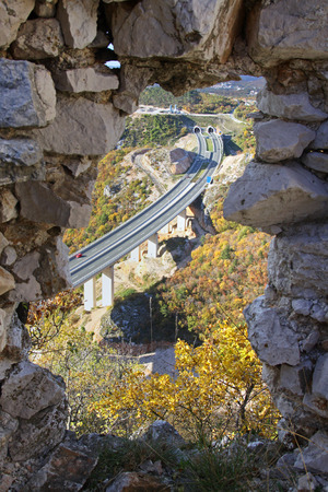 Highway bridge and tunnel through autumn scenery viewed through a hole in a castle wall Croatia.の写真素材