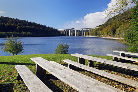 Wooden beches in a park by a lake on a sunny spring afternoon with a highway bridge in the background.の写真素材