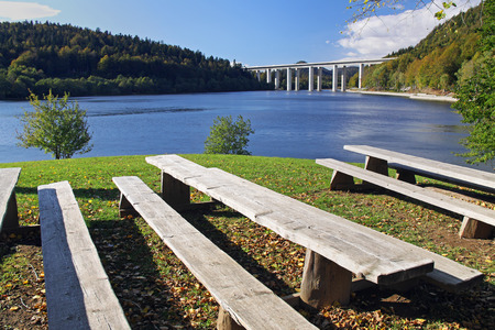 Wooden beches in a park by a lake on a sunny spring afternoon with a highway bridge in the background.の写真素材