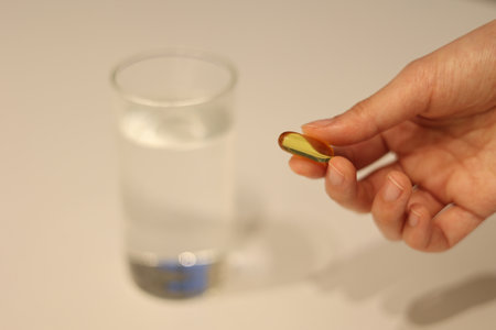 Woman is taking medicine with cup of water on the white table, girl is taking nutritional supplement...