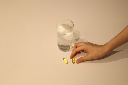 Woman is taking medicine with cup of water on the white table, girl is taking nutritional supplement by handの写真素材