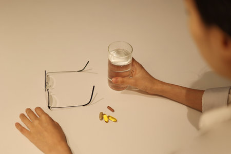 Woman is taking medicine with cup of water on the white table, girl is taking nutritional supplement by handの写真素材