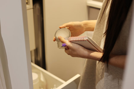 Woman is holding cosmetic jar and a notebook, worker is taking inventory in a warehouseの写真素材