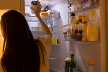 The woman is taking a bottle from the refrigerator in the kitchenの写真素材
