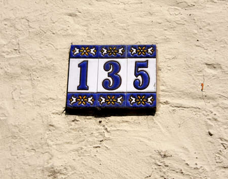 Decorated blue and white house / address number 135, hung on a bright, rough wall. Decorative number plateの写真素材