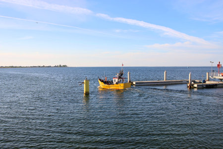 A yellow boat sailing out into the Baltic Sea from the port in Mechelinki in Poland. Boat in the sea at sunsetの写真素材