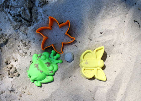 Yellow, green and orange sand molds lie on the beach on a sunny day. Sand sprinkled into a mold. There is a stone in the middle.の写真素材