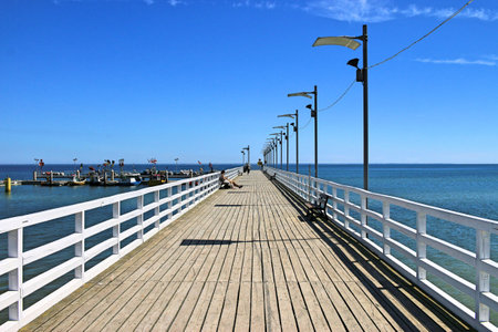 Wooden pier on the Baltic Sea in Mechelinki on a sunny day. Cloudless blue sky. In the background, the blue sea and the port of fishermen in mechelinki. June 2021, Mechelinki, Polandのeditorial素材