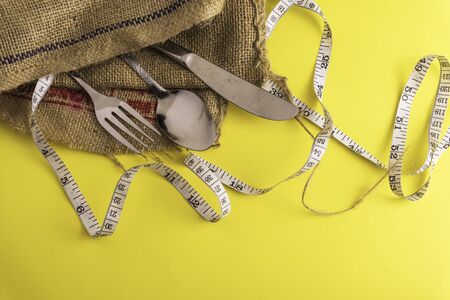 Fork, spoon,knife and measurement tape with yellow background, diet or healthy eating concept. Soft...