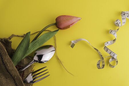 Fork, spoon and flower with a measuring tape and yellow background, diet or healthy eating concept....