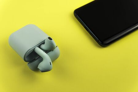 Bluewireless earphones or headphones, plastic case or box for storage and charging and smartphone on...