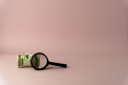 USD upon closer inspection with a magnifying glass becomes 100 USD, isolated on pink backgroundの写真素材