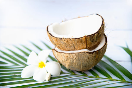 Coconuts with halves of coconut and plumeria flower on white wooden background. Space for text.