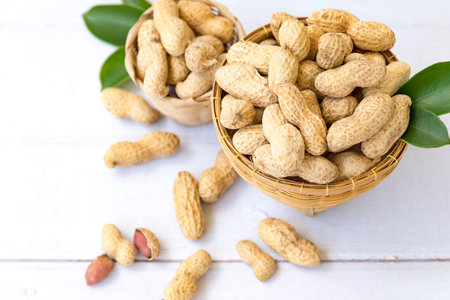 Peanuts with leaf in wooden basket and peanuts in the peel scattered isolated on wooden white...