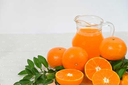 A pitcher of freshly squeezed orange juice, orange slices with whole oranges, and orange leaves, all organic, set against a white background.の写真素材