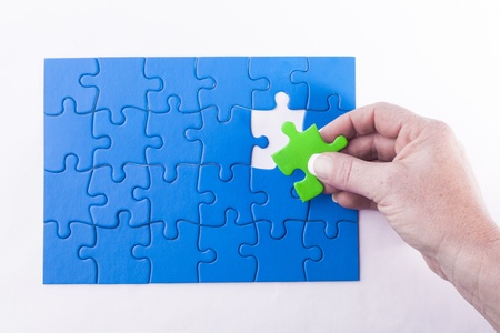 Woman's hand placing green Jigsaw puzzle piece in blue puzzles signifying diversity and equalityの写真素材
