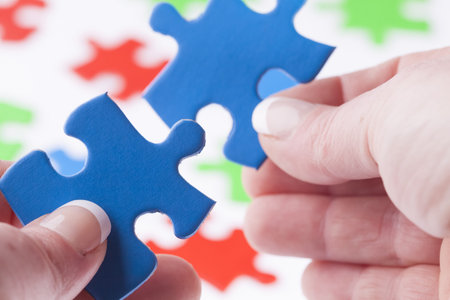 Womans hands fitting jigsaw puzzle pieces together, close up with shallow depth of field