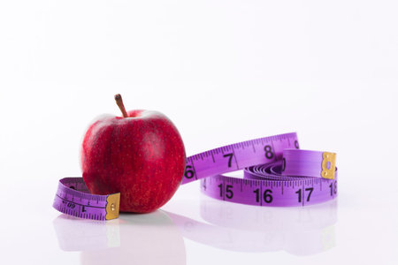 red apple with tape measure on white background signifying weight loss and healthy eatingの写真素材