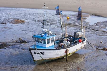 Battered fishing boat at low tide in harbour with ragged flags at Folkestone, Kent, UKのeditorial素材