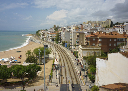 Seaside railway track in Spain with traditional architecture, people, sandy beach and the sea for travel and tourismのeditorial素材