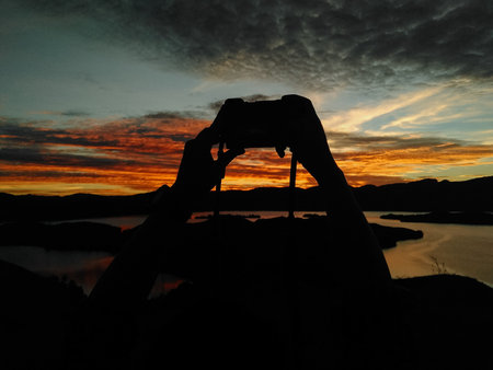 Silhouette of a woman taking a photo with a camera at sunsetの写真素材
