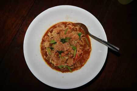 Thai spicy noodle with pork in white dish on wooden tableの写真素材