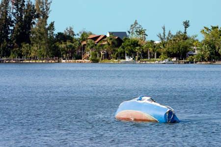Sunken and abandoned sailboat backdropped with impressive waterfront homesの写真素材