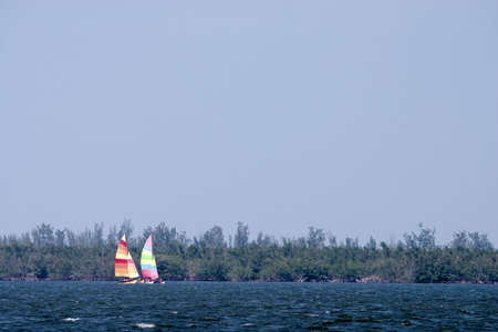 Two brightly colored sailboats on a windy blown choppy riverの写真素材