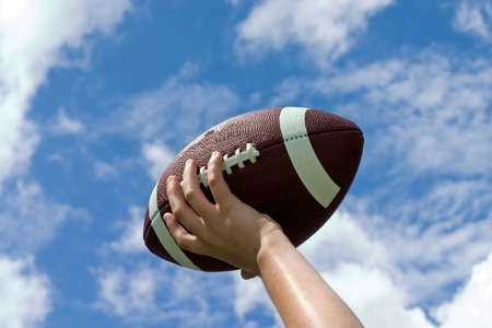 Football in childs hand against blue sky with puffy cloudsの写真素材