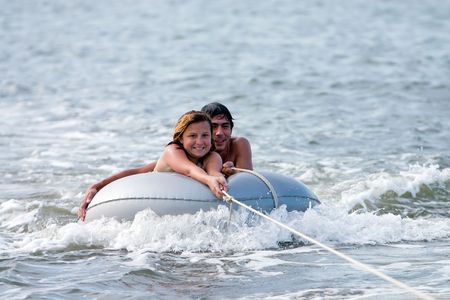 Man and girl on tube in water being towed by boat.の写真素材