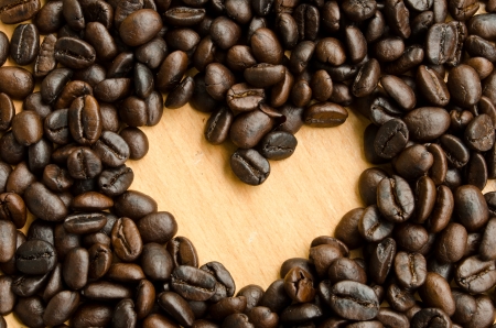 Heart shape made from coffee beans on wooden surface.の写真素材