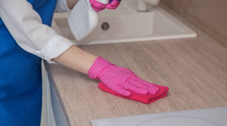 A girl in pink rubber gloves washes a cabinet surface with a microfiber clothの写真素材