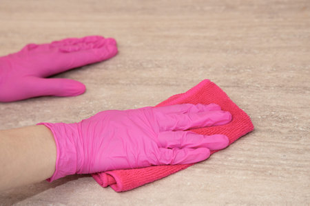 A girl in pink rubber gloves washes a wooden surface with a microfiber cloth.